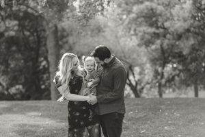 Black and white photo of a family sharing a tender moment together outdoors in a park setting.