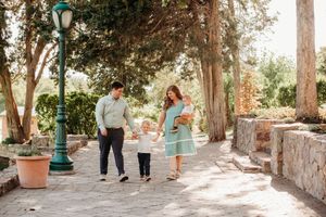 A couple walks hand in hand down a tree-lined stone path with green lamp posts and terracotta planters.