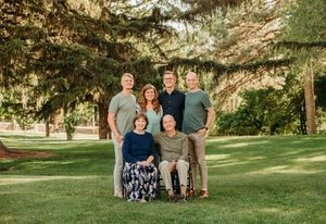 A group poses together on a sunny lawn with evergreen trees in the background during golden hour.