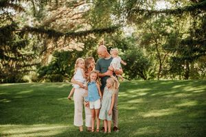 A family wearing coordinated blue and white outfits poses together in a sunlit garden setting during a photo session.
