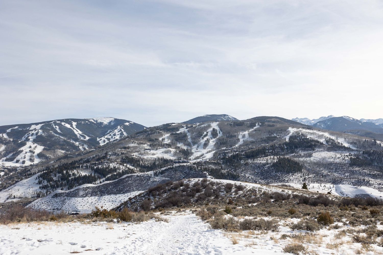 Snow-covered mountain peaks and ski slopes at a winter resort with cloudy skies in the background.