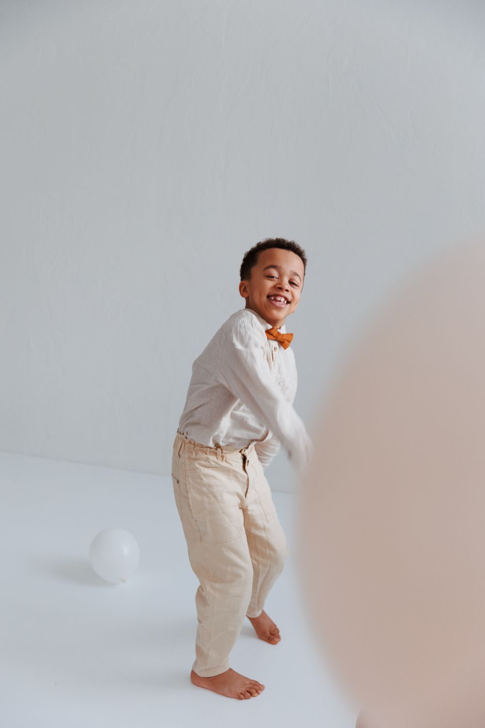 A small child in white shirt and beige pants dances joyfully against a light background.