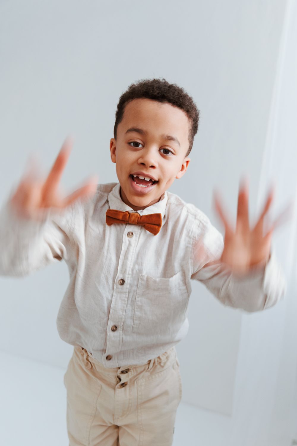 A young child in a white button-down shirt and bow tie makes playful hand gestures against a light background.