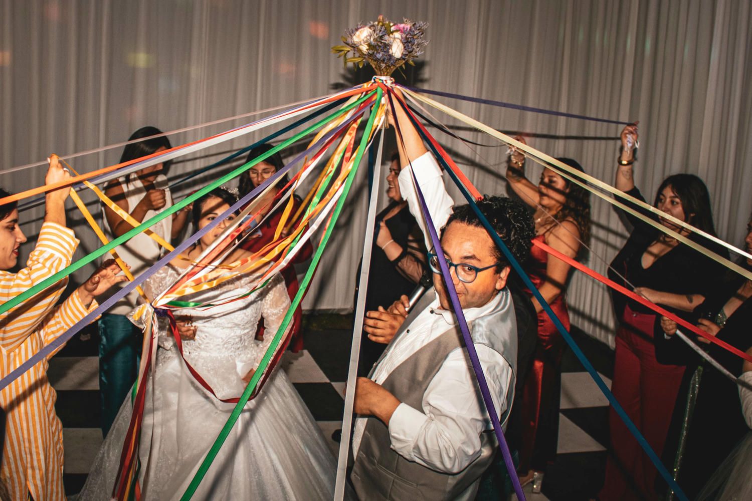 Gran grupo de invitados bailando en recepción de matrimonio en espacio interior con decoración blanca.