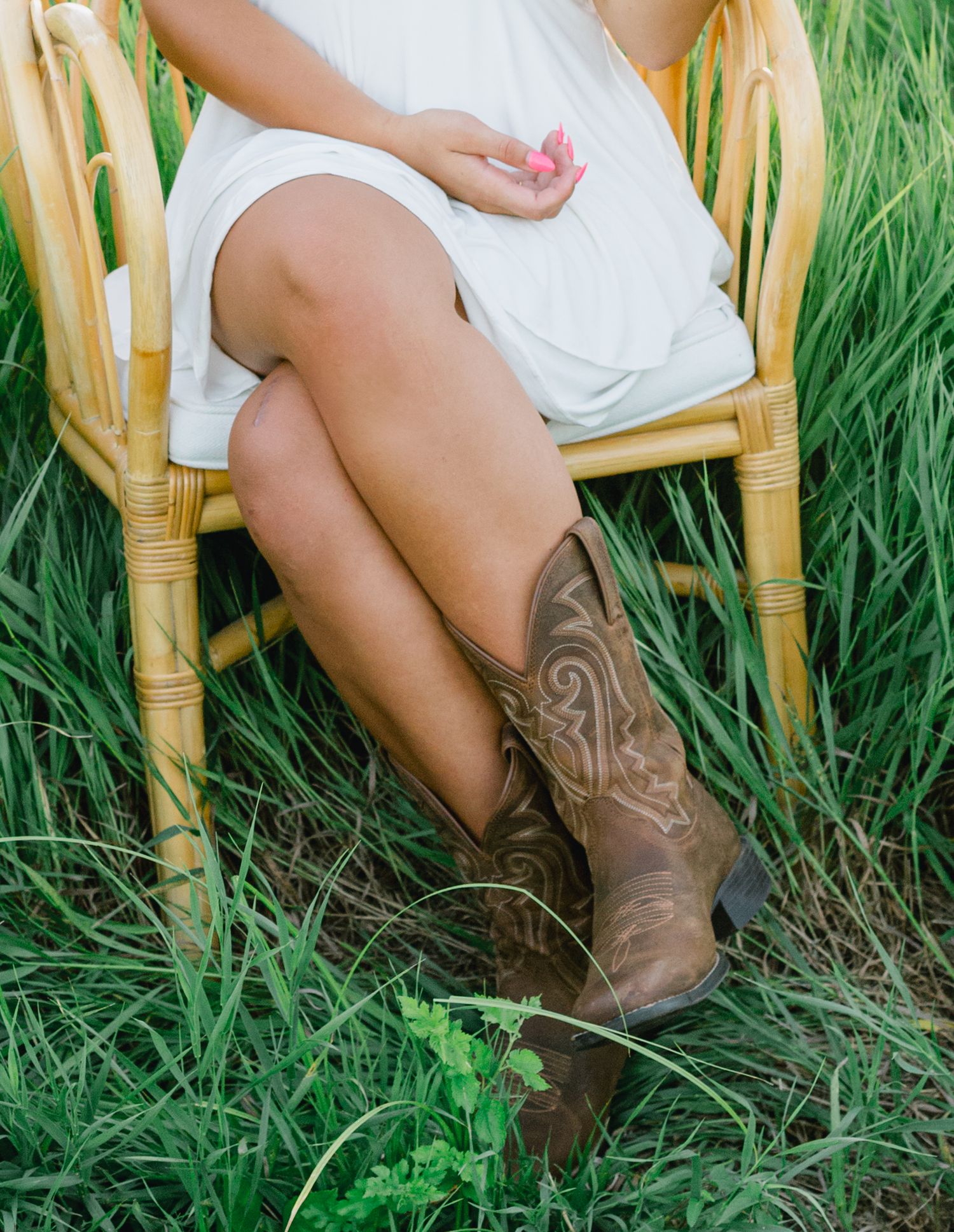 Brown cowboy boots and white dress worn by a high school senior girl are shown against lush green grass at Wanatee Park in Marion, IA.