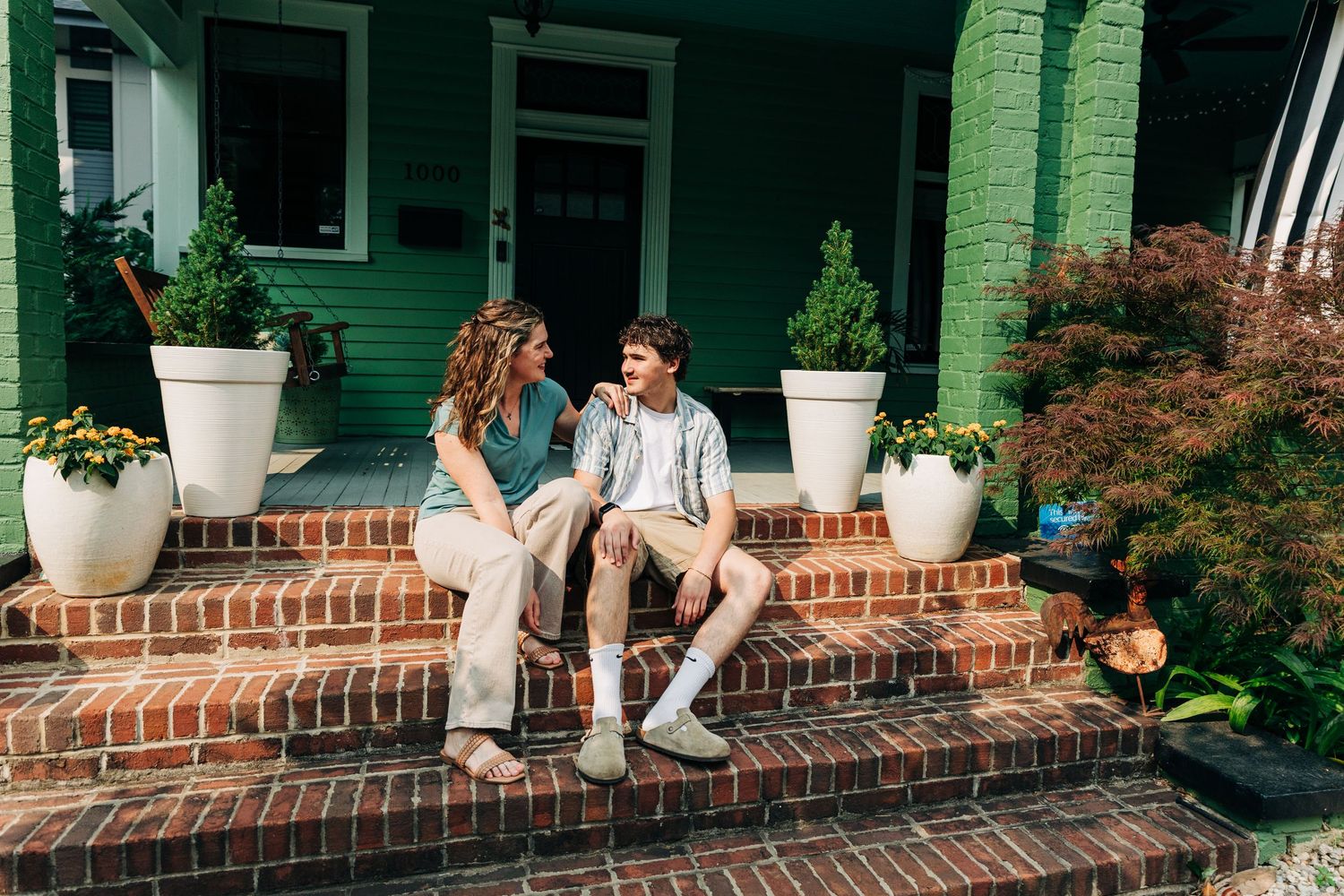 A family sits together on brick steps of a green house during a Charlotte family photo session