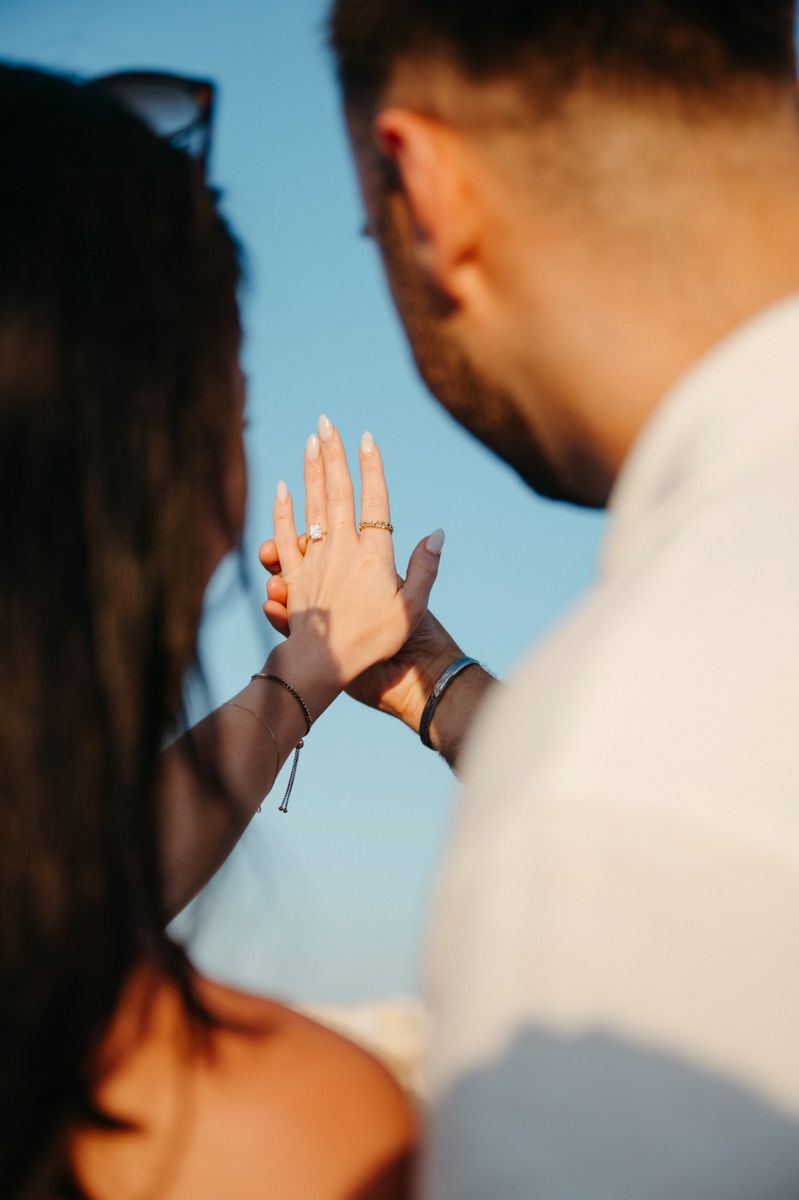 Two hands reach towards each other against a blue sky background, with sunlight creating a soft glow between them.
