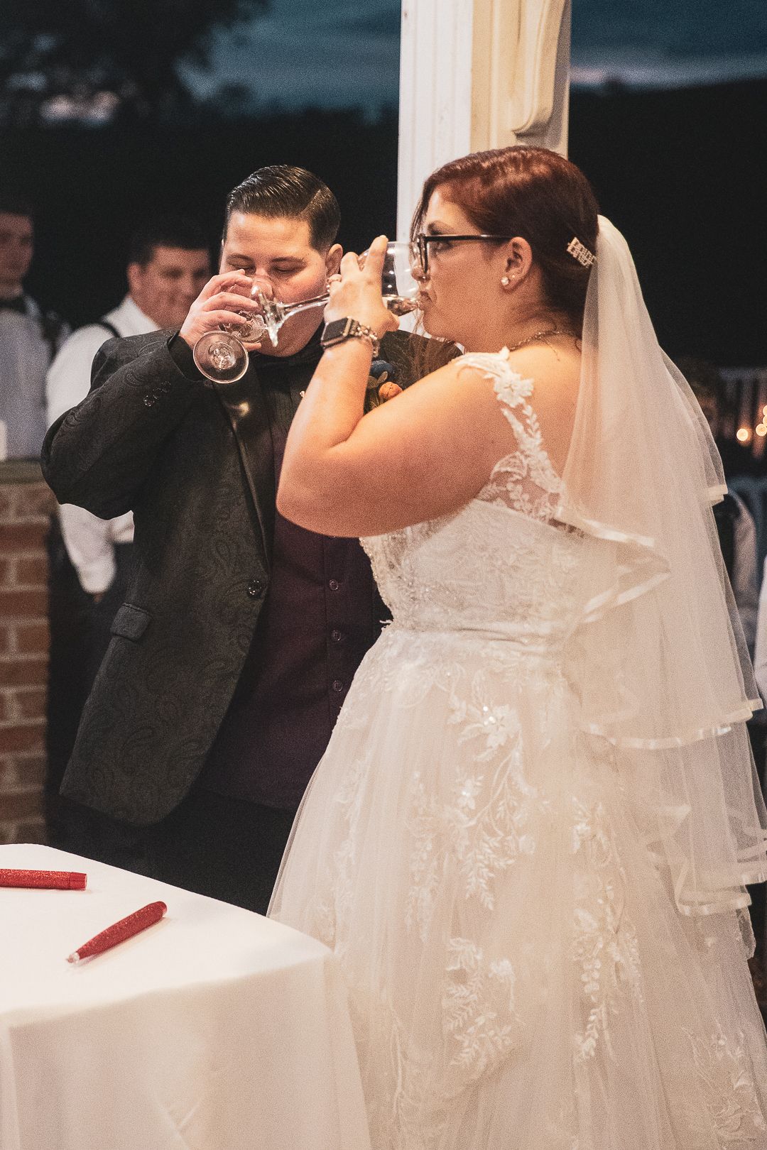 Newlyweds in formal attire share a celebratory drink together during their wedding reception.