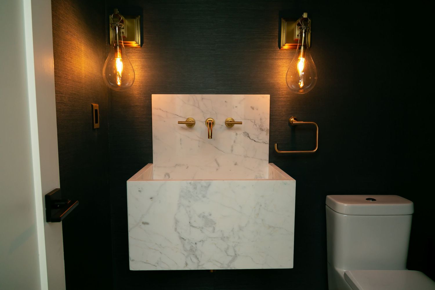 Modern bathroom with floating marble sink and industrial brass wall sconces.