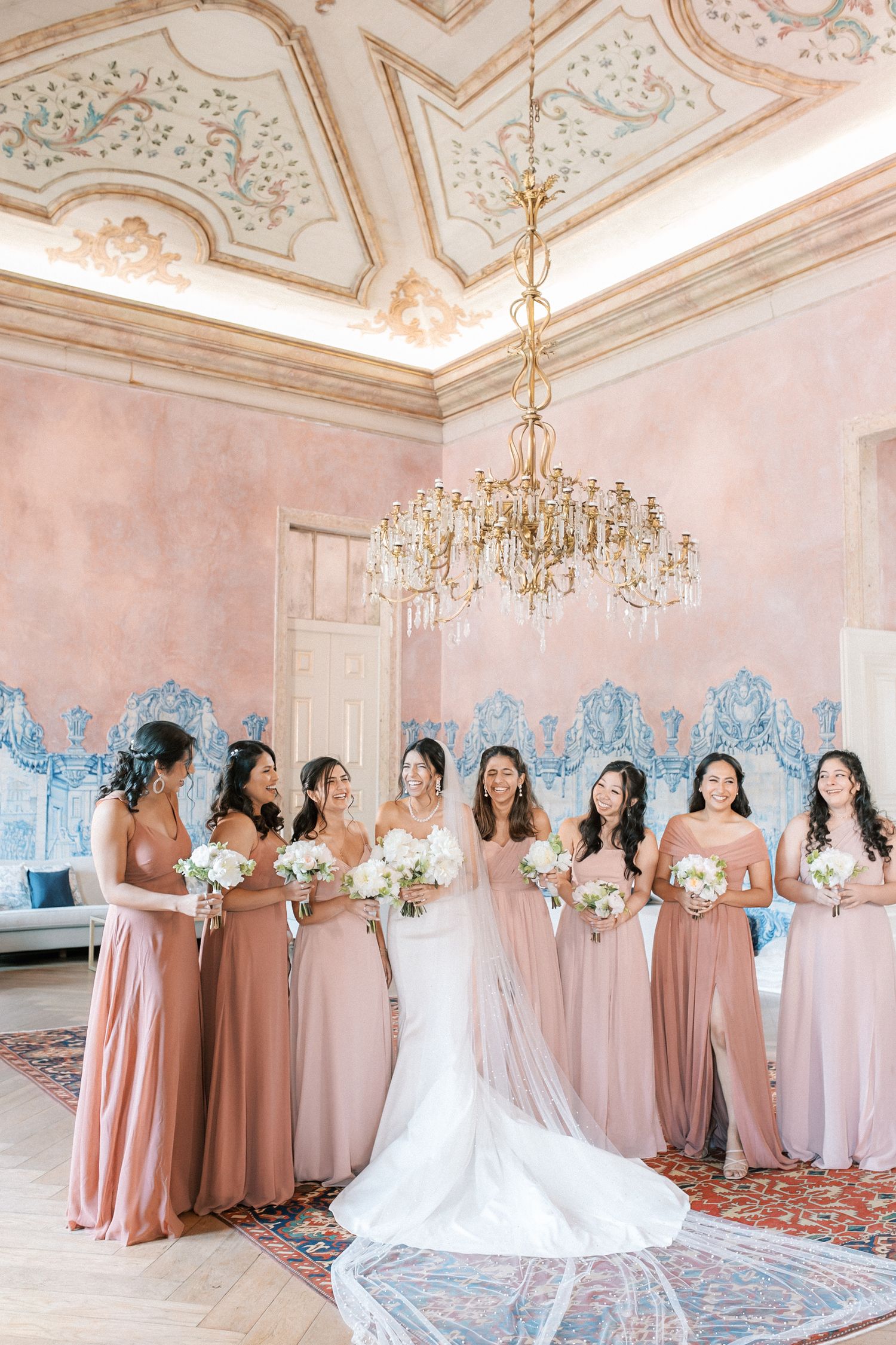 Bride with bridesmaids in blush dresses inside Palácio de Fronteira room with chandeliers and tiles