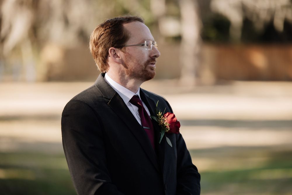 A wedding ceremony takes place outdoors with the couple and officiant standing together during a joyful moment.