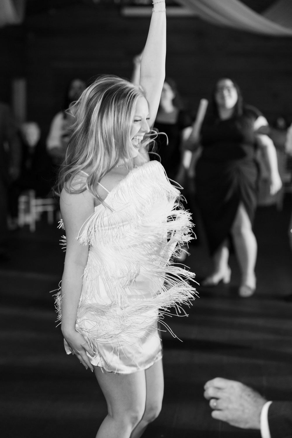 A dancer in a white feathered dress twirls gracefully in a dark performance space.