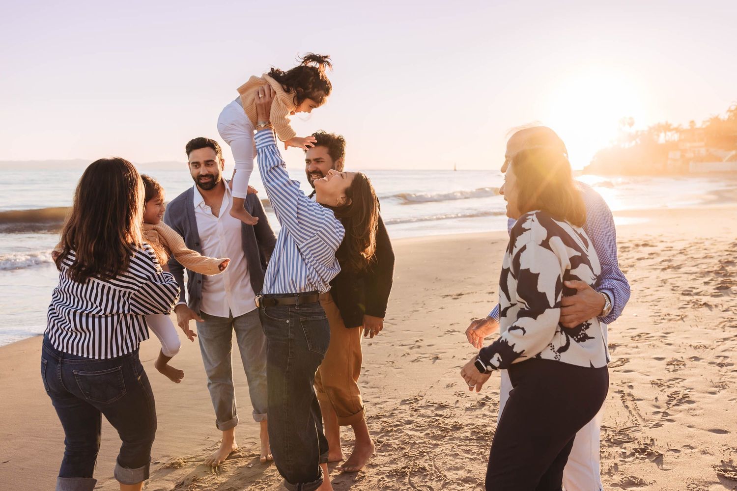 Group of people walking and laughing together on a sandy beach at sunset with warm golden light.
