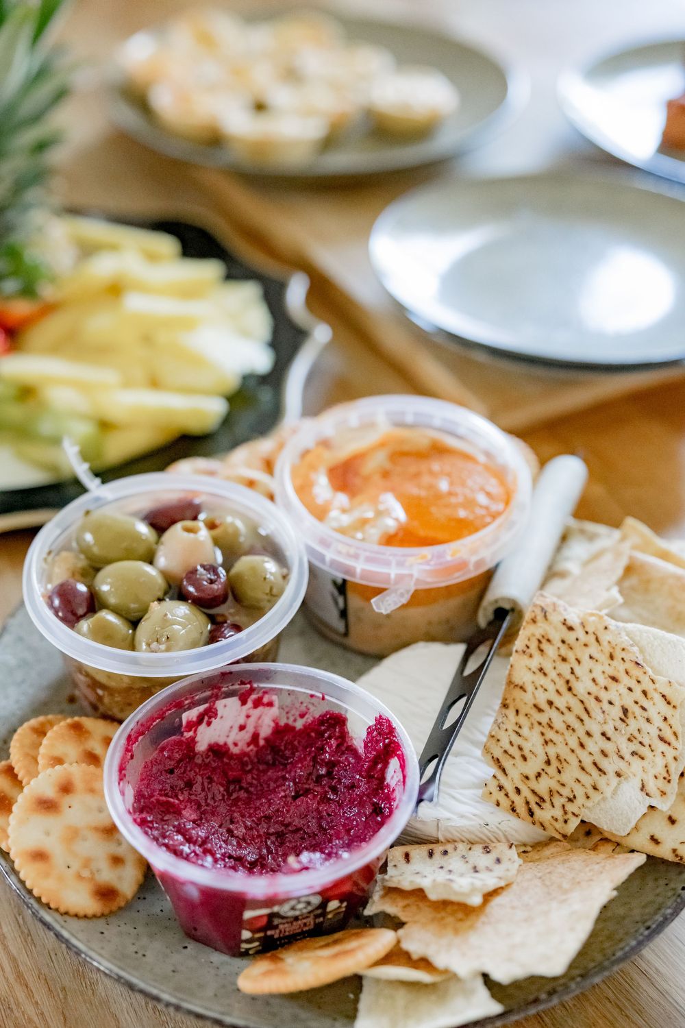 Appetizer platter with olives, dips, crackers and fresh fruit arranged on a wooden board.