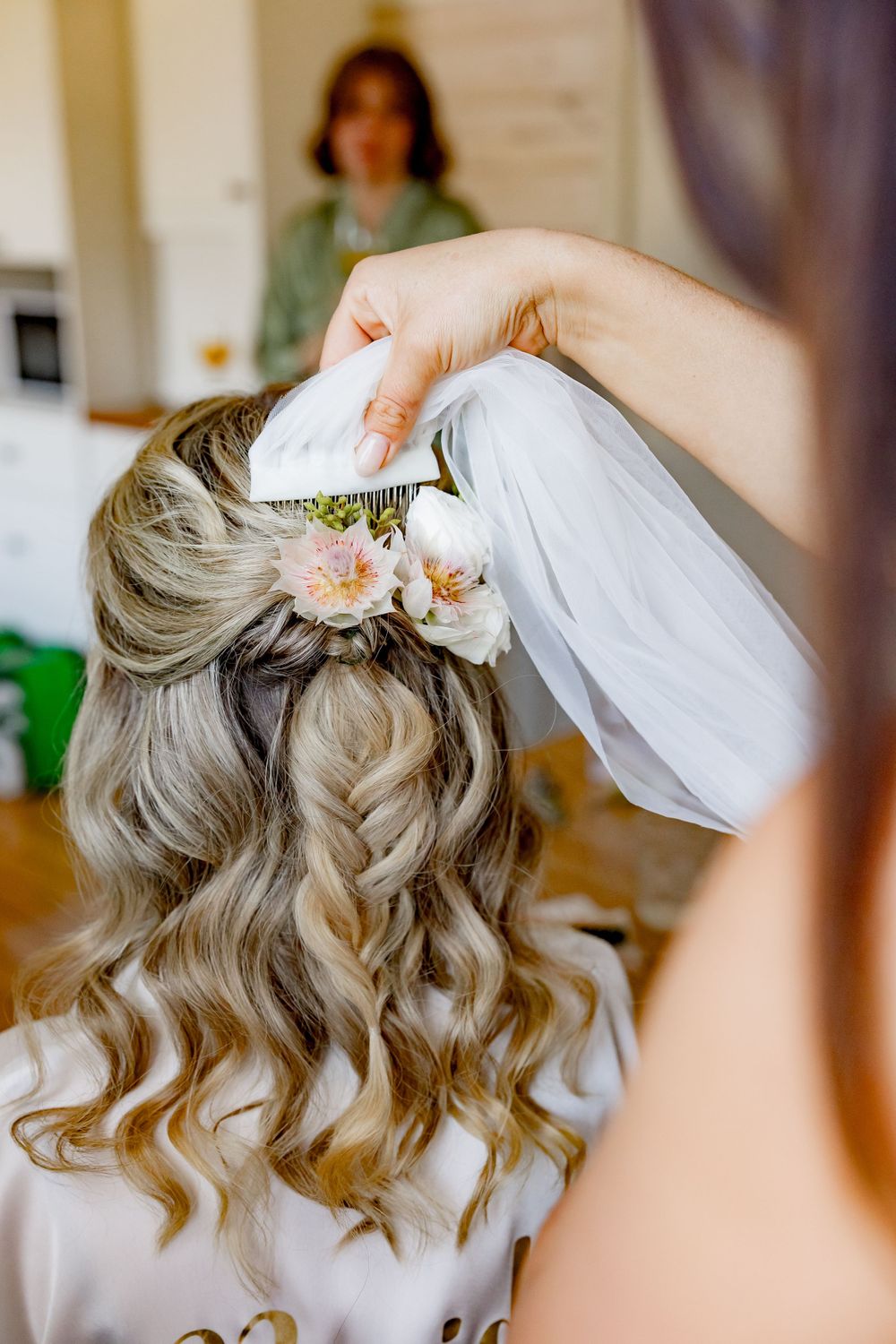 Close-up of wavy bridal hairstyle with flowers and veil being styled.