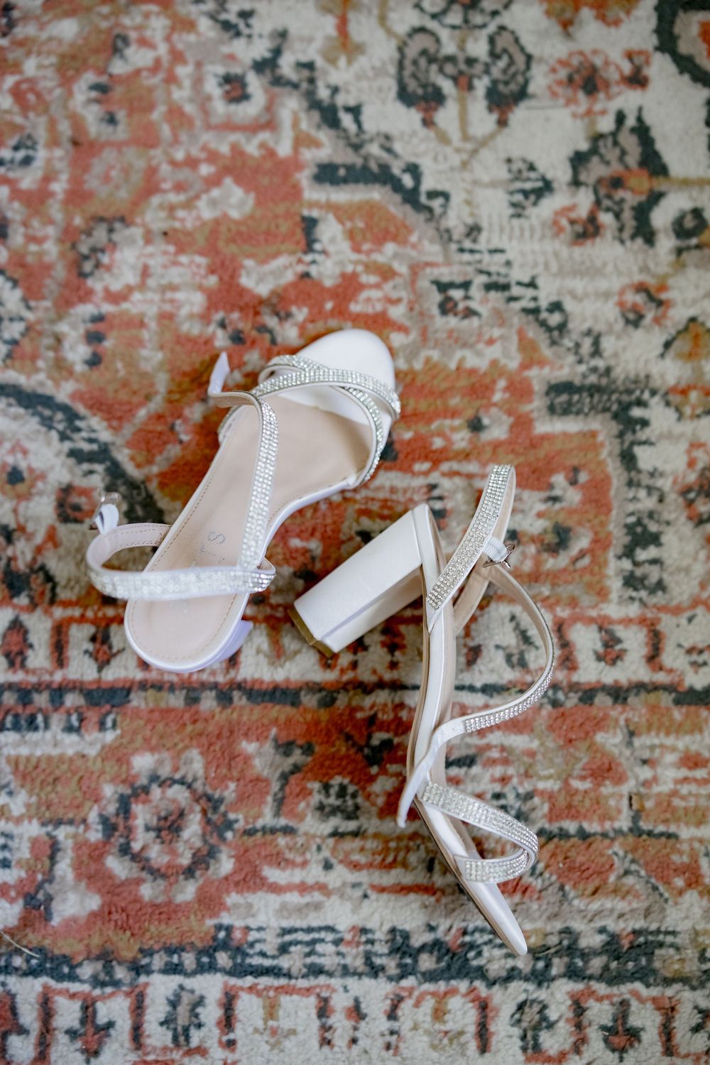 White strappy bridal sandals on ornate vintage-style rug.