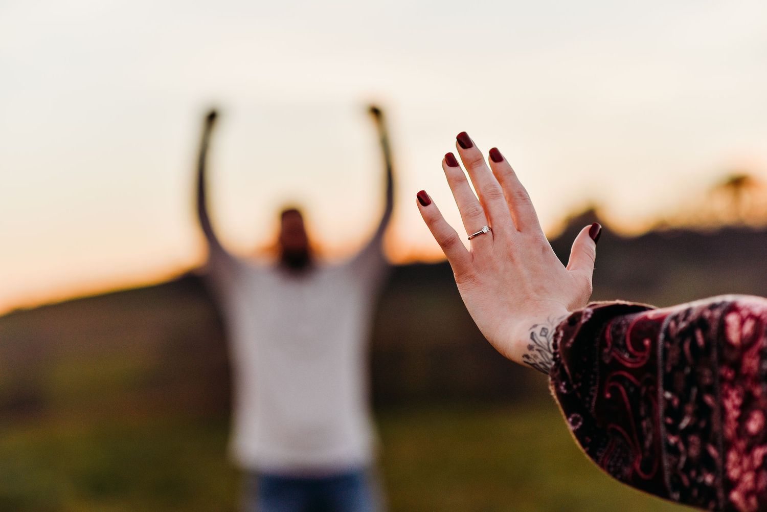 woman shows off her ring while her partner celebrates in the background