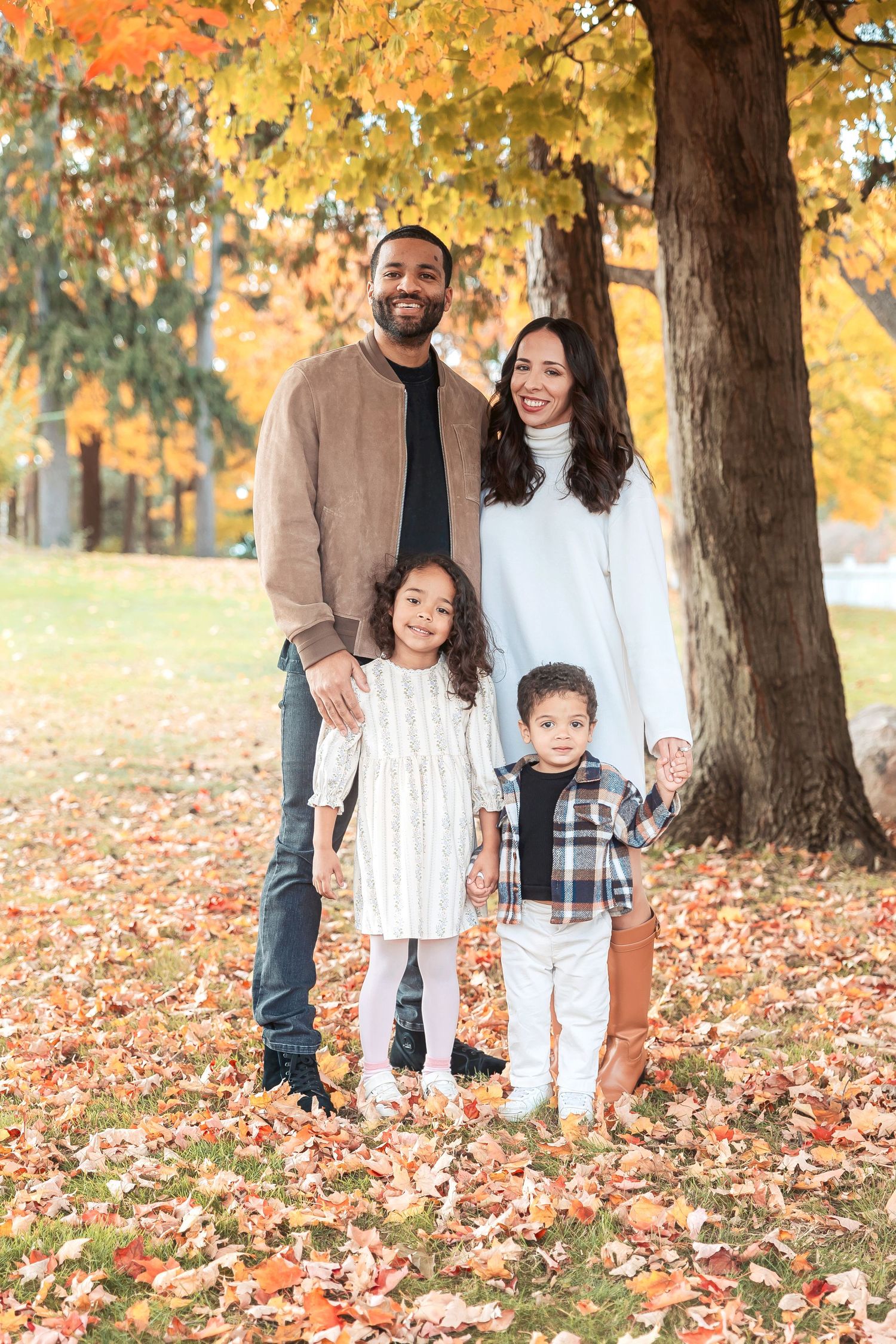 A family of four poses under trees with golden autumn leaves in a park setting. Michigan Detroit Novi Northville Portrait Photographer