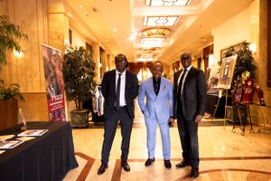 Three people in formal attire stand together at an event with display tables.