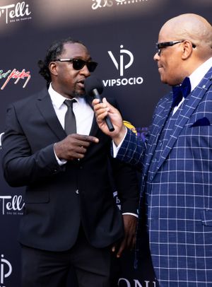 Two people in suits having an interview on red carpet with VIPSocio backdrop.