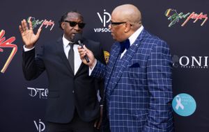 Two men in suits having animated conversation on red carpet with event backdrop.