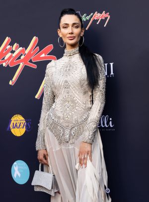 A long white embellished dress with intricate beading is shown against a dark backdrop.
