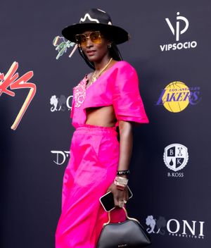 Person in hot pink outfit with hat poses against VIPSocio and Lakers branded backdrop.