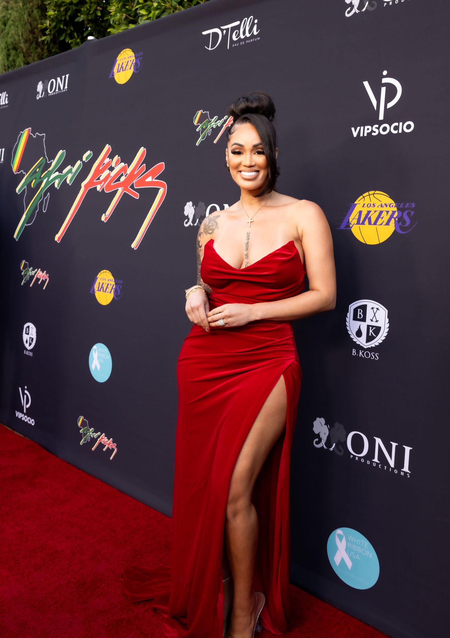 Woman in red velvet gown poses on red carpet with Lakers and VIP Socio event backdrop.