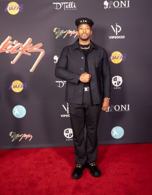 Man in all-black outfit poses on red carpet with Lakers and event sponsor logos.