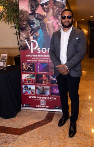A person in a dark suit and sunglasses stands confidently next to a promotional banner for social events.