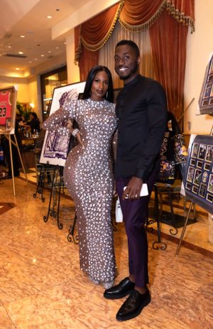Two people pose together at event, one wearing animal print dress and other in dark suit.