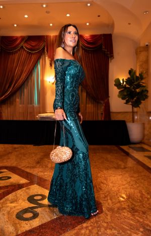 An elegant teal sequined evening gown with a small golden clutch is displayed at a formal event.