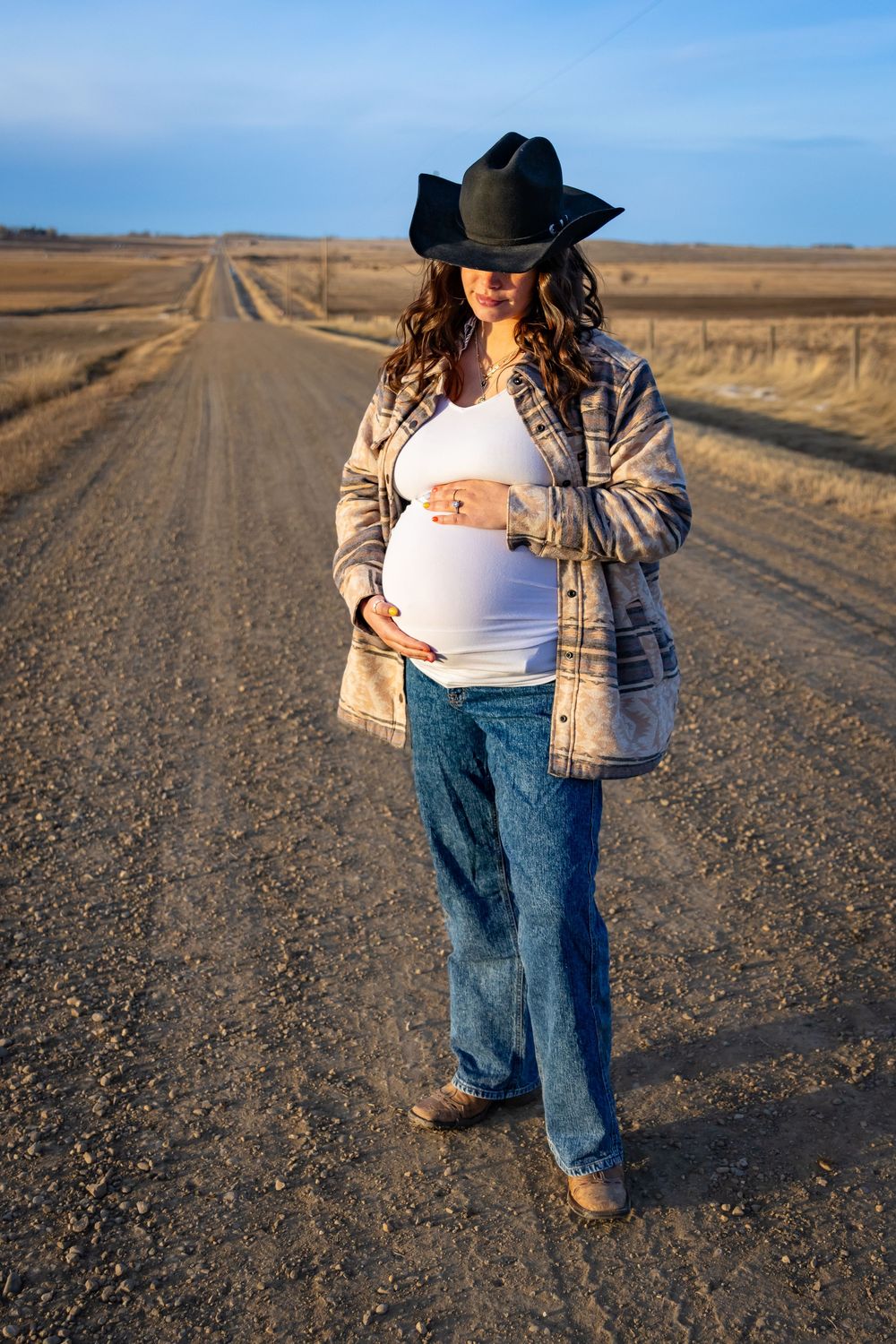 a pregnant woman in a cowboy hat on a dirt road showing her baby bump.