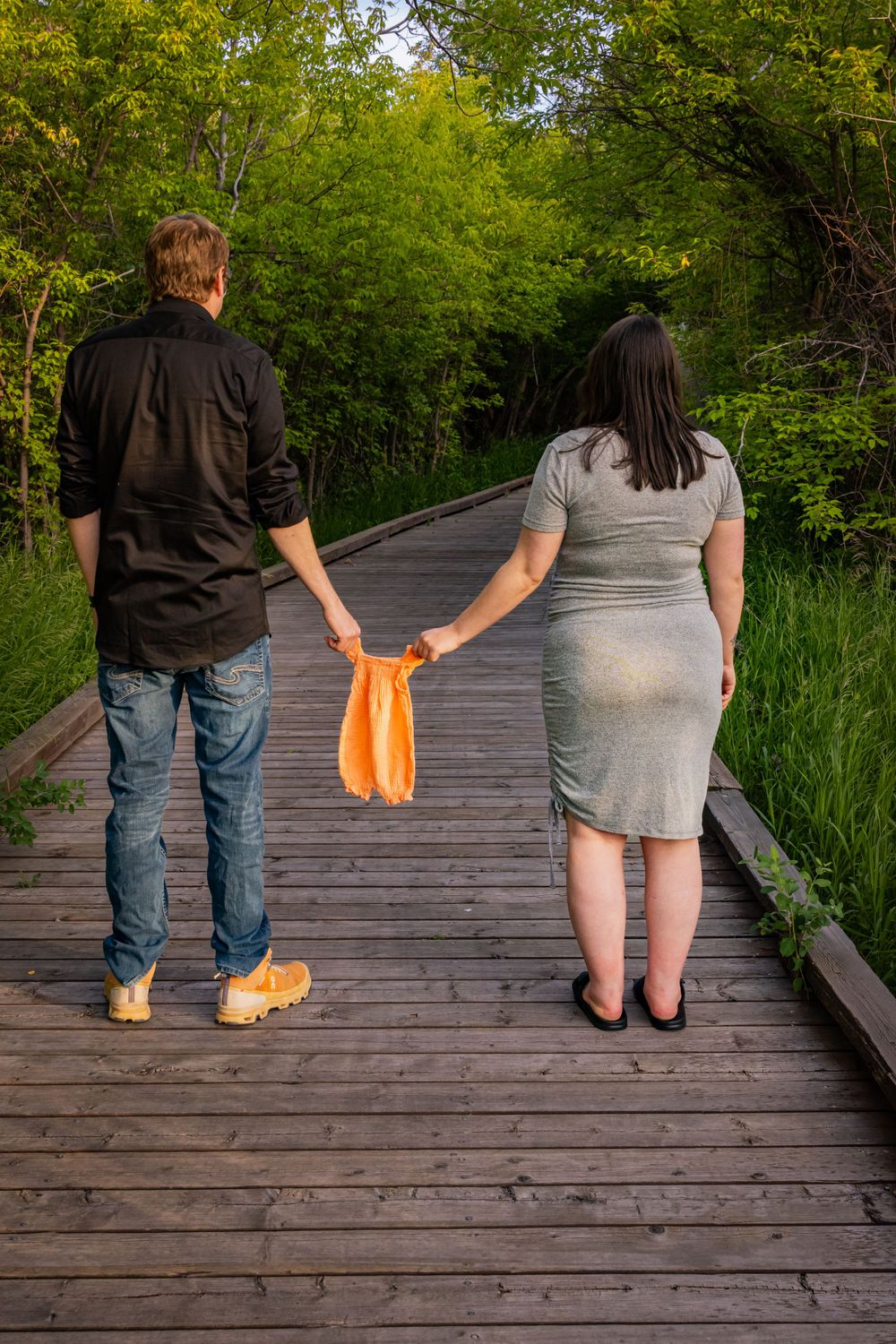A couple holding a baby onesie on a bridge.