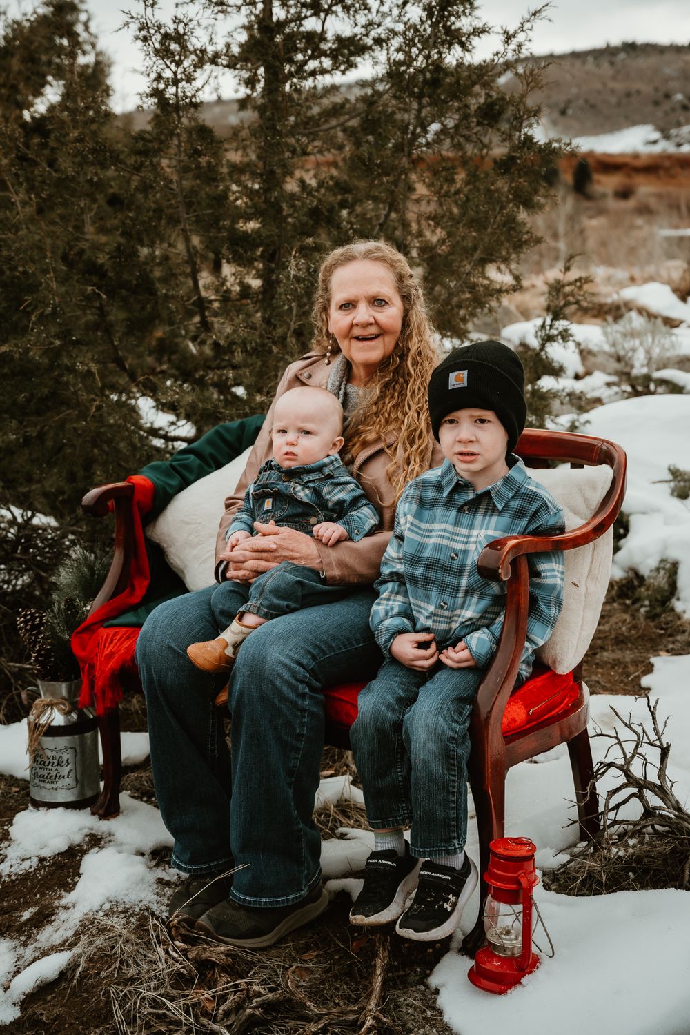 Family relaxing on a red couch outdoors in the snow surrounded by evergreen trees.