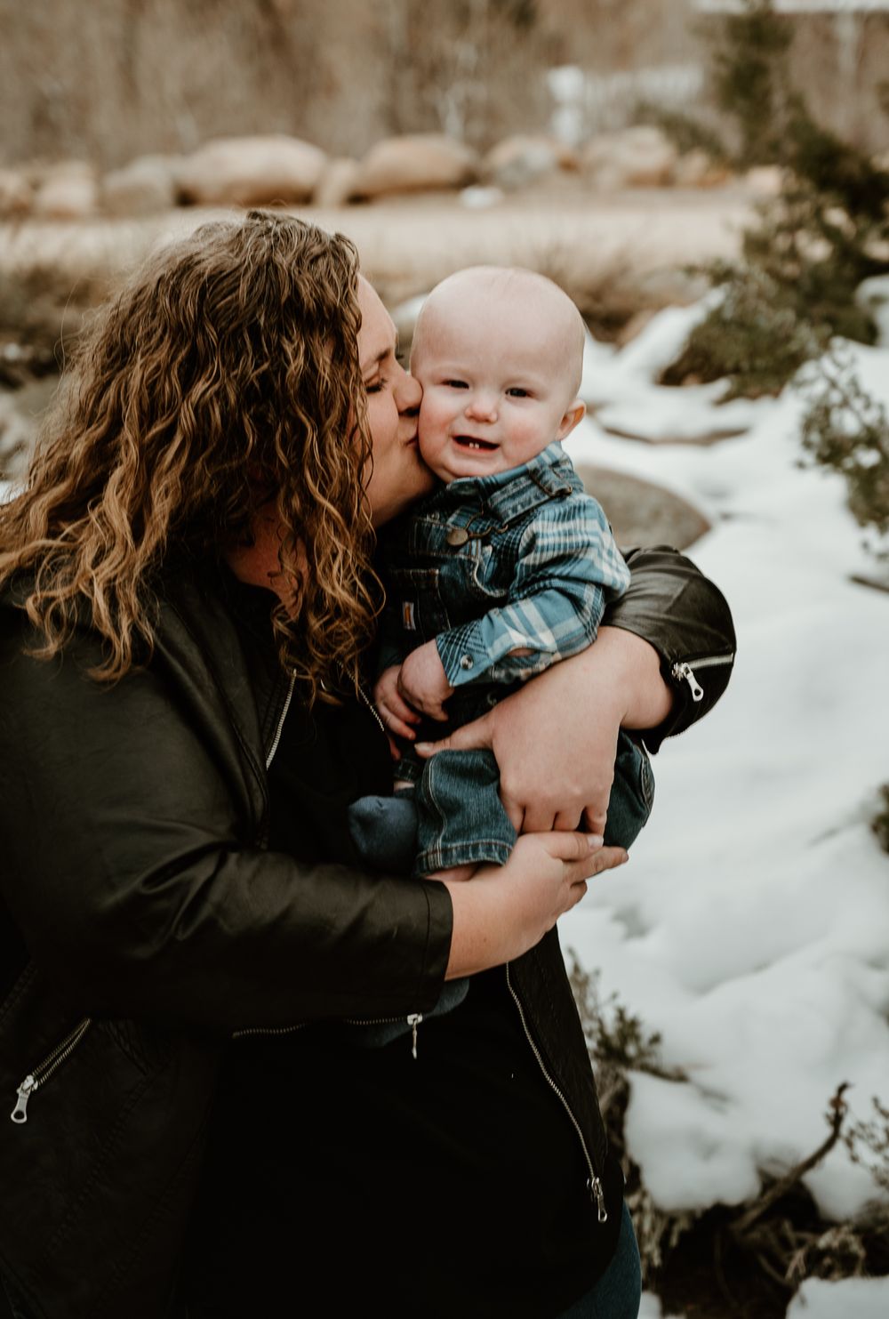 Sepia-toned winter portraits capture loving interactions between parent and infant against snowy backdrop.