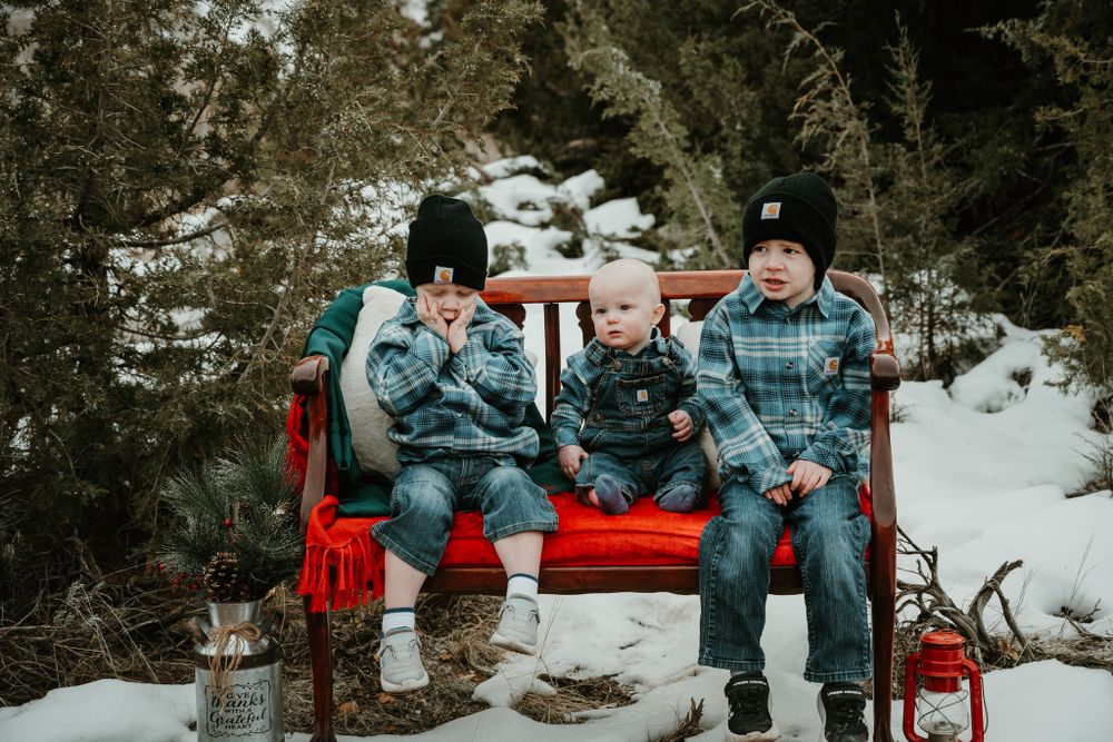 Family sitting together on red bench during winter photoshoot in snowy outdoor setting.