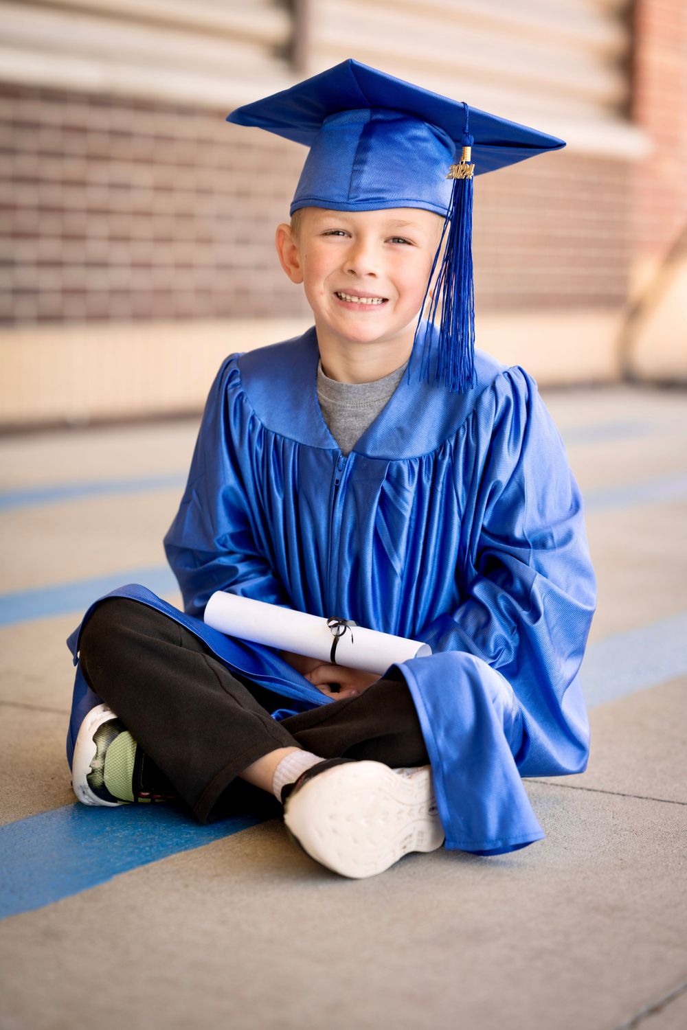 Graduate in blue cap and gown lies on concrete for playful photo.