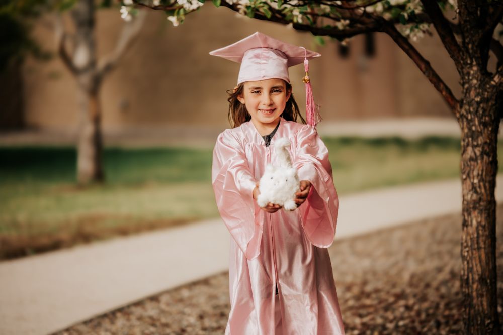 Person in flowing pink dress poses under blooming cherry blossom trees.