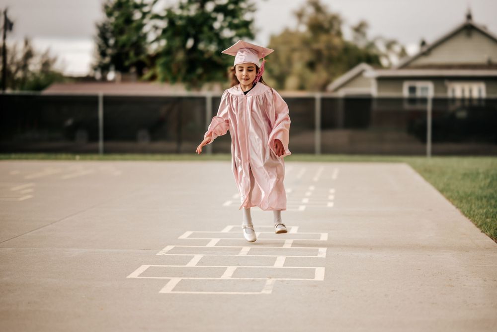 Person in pink dress jumps and plays on outdoor hopscotch court.