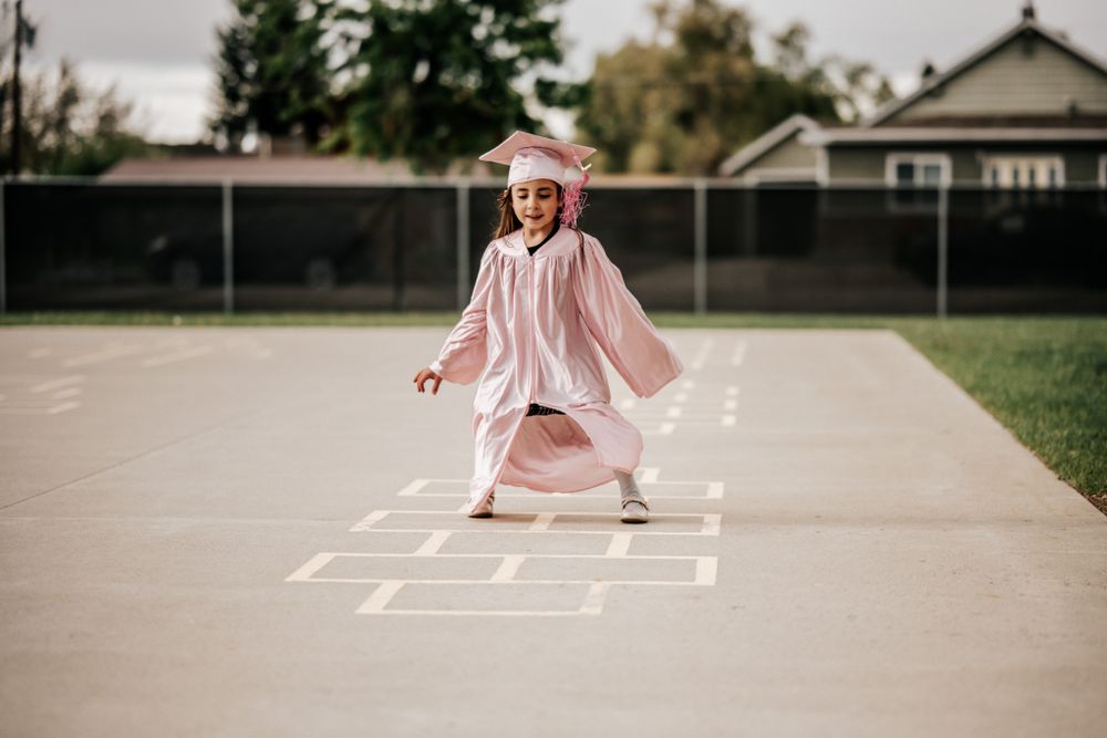 Child plays hopscotch on playground wearing flowing pink dress.