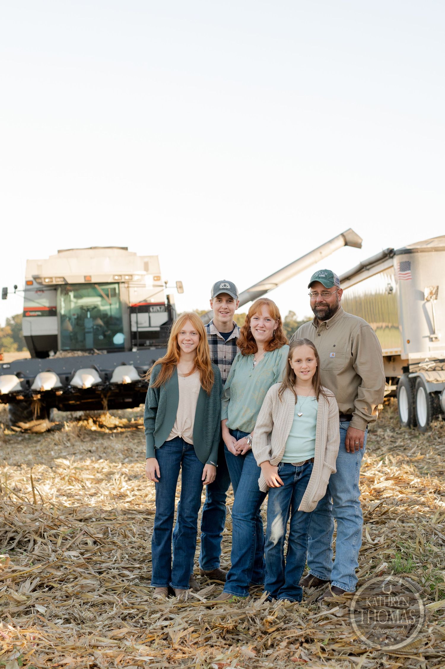 A family poses together in front of harvesting equipment on their farm at sunset.