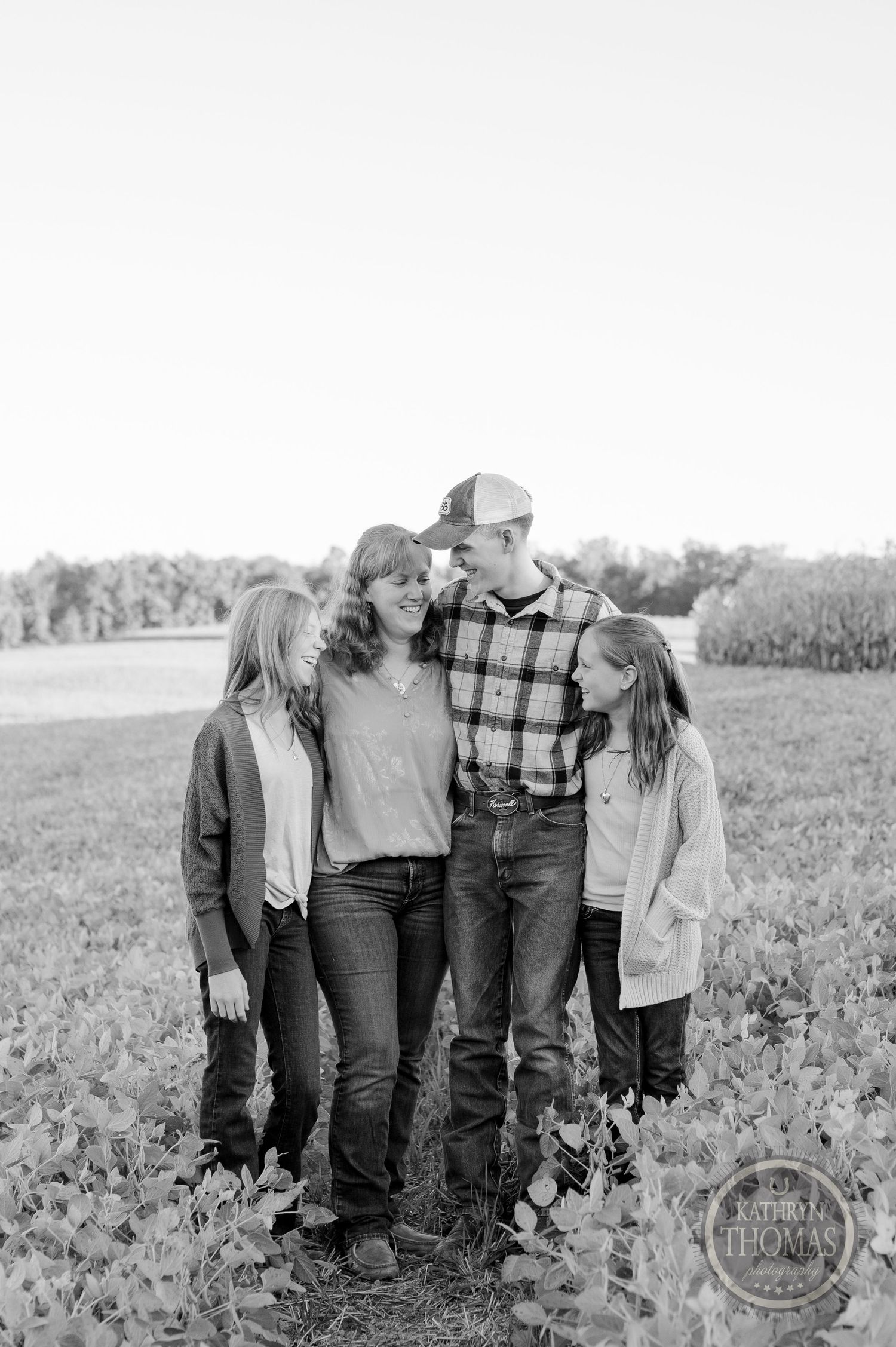 A black and white portrait of a family standing close together in a rural field setting.