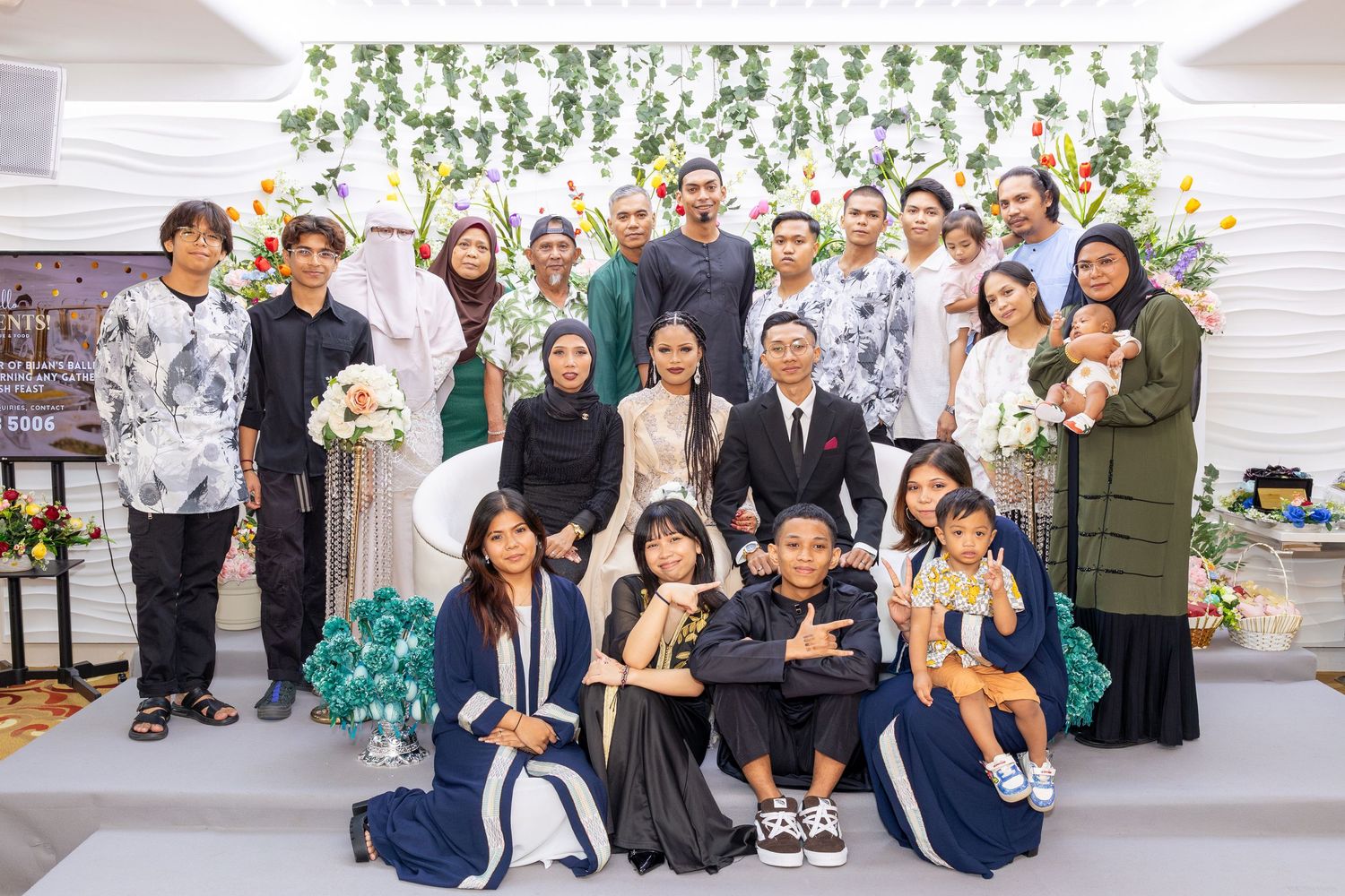 Large group photo of wedding guests and celebrants in front of floral wall.