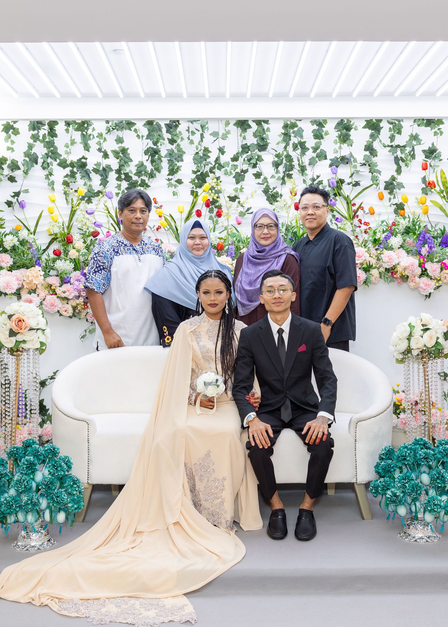 Family group photo at a wedding with floral backdrop and elegant cream-colored decor.