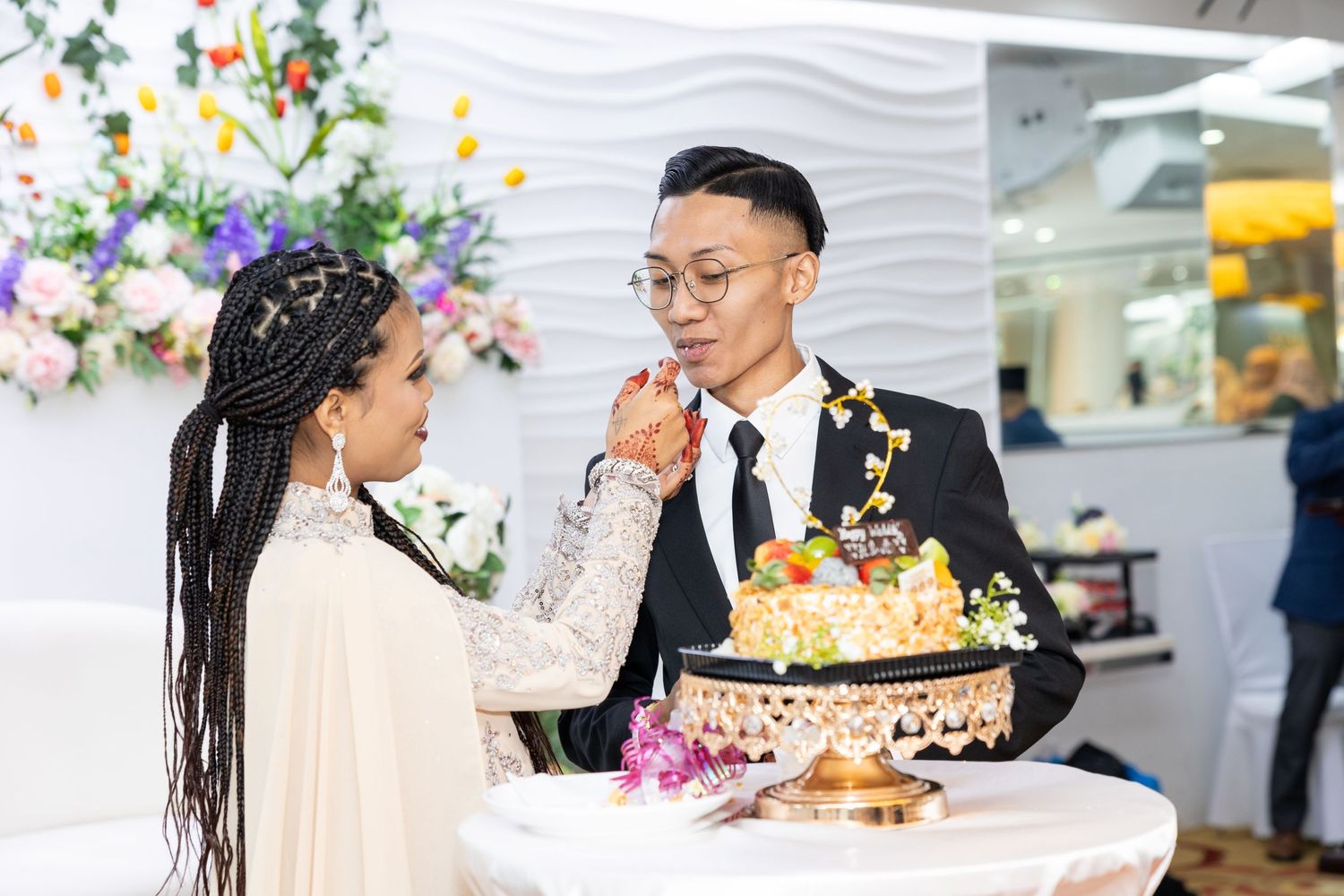 Wedding couple sharing cake at reception with floral decorations.