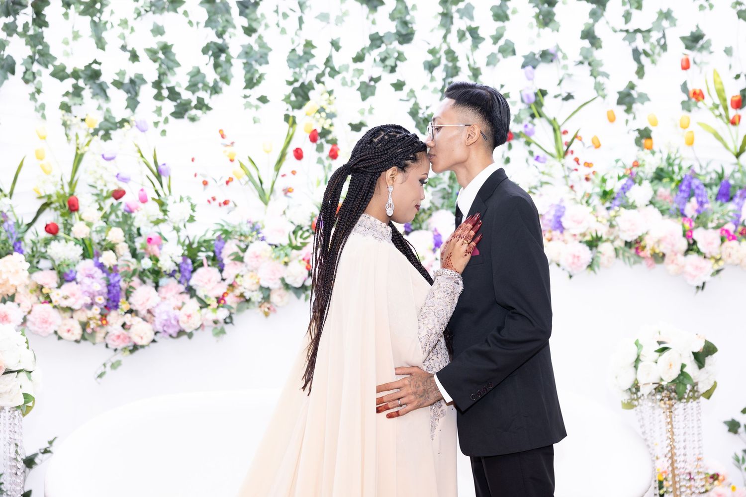 A romantic wedding portrait against a floral backdrop features a couple sharing an intimate moment together.