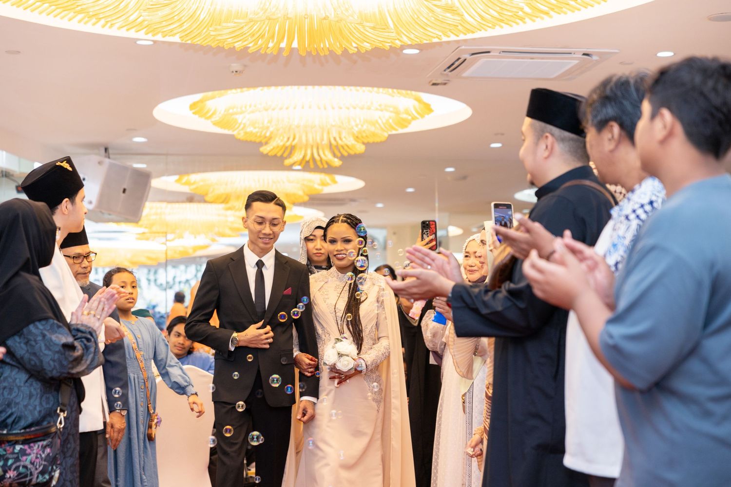 Wedding guests take photos during a reception as confetti falls in an elegantly lit ballroom.