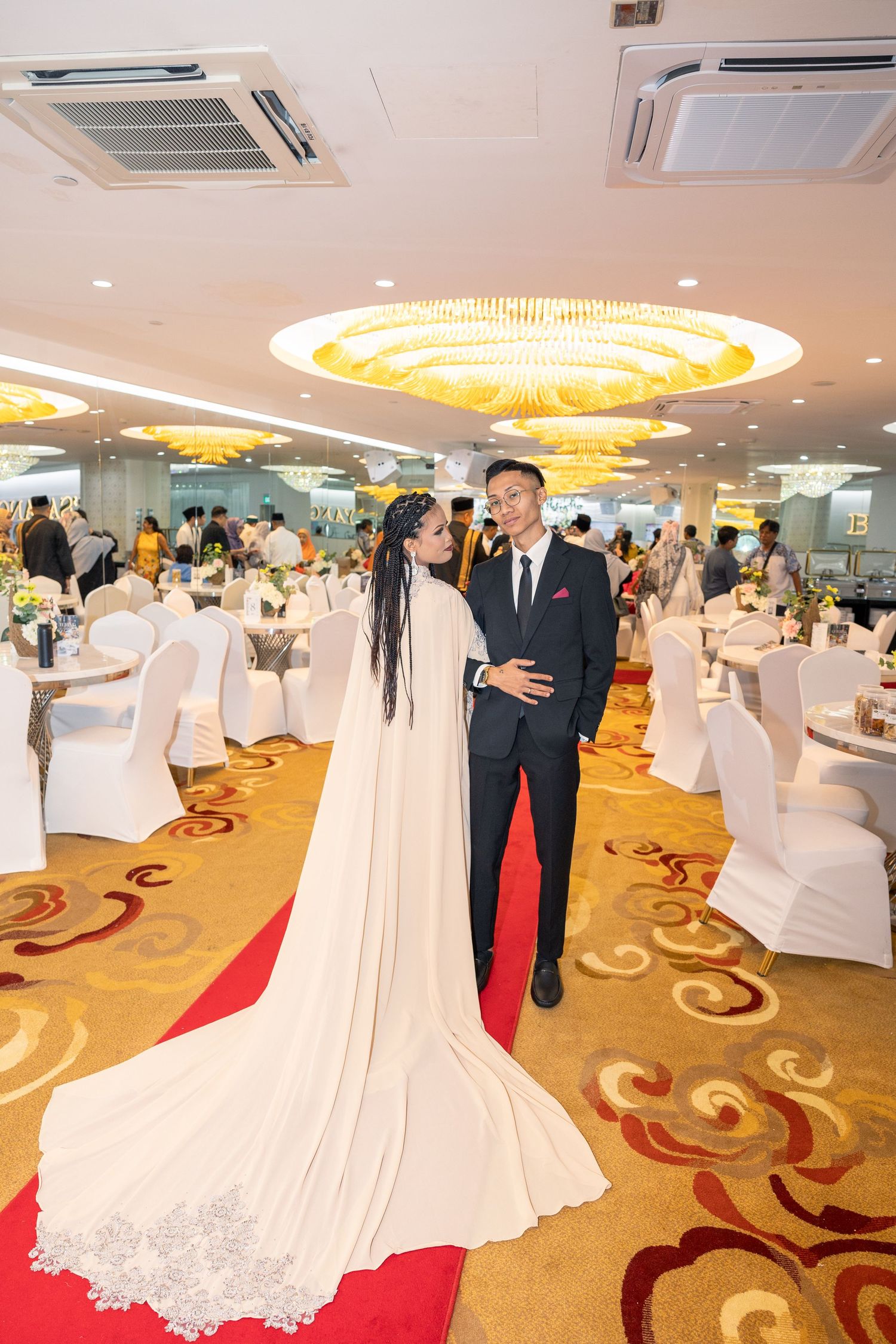 A wedding couple poses in an elegant ballroom with dramatic lighting and decorative carpet.