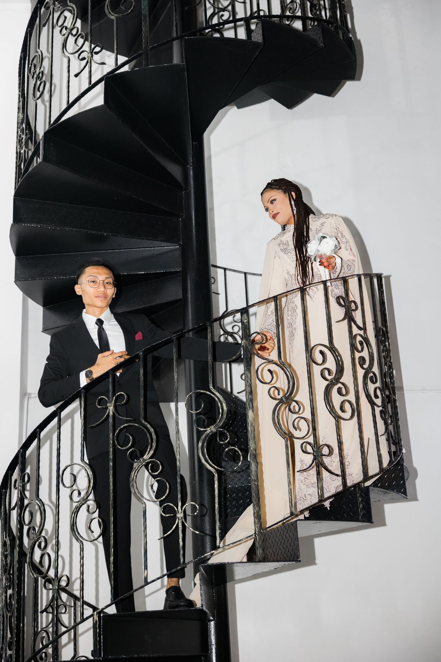 A stylish couple poses on a spiral staircase in contrasting black and white formal attire.